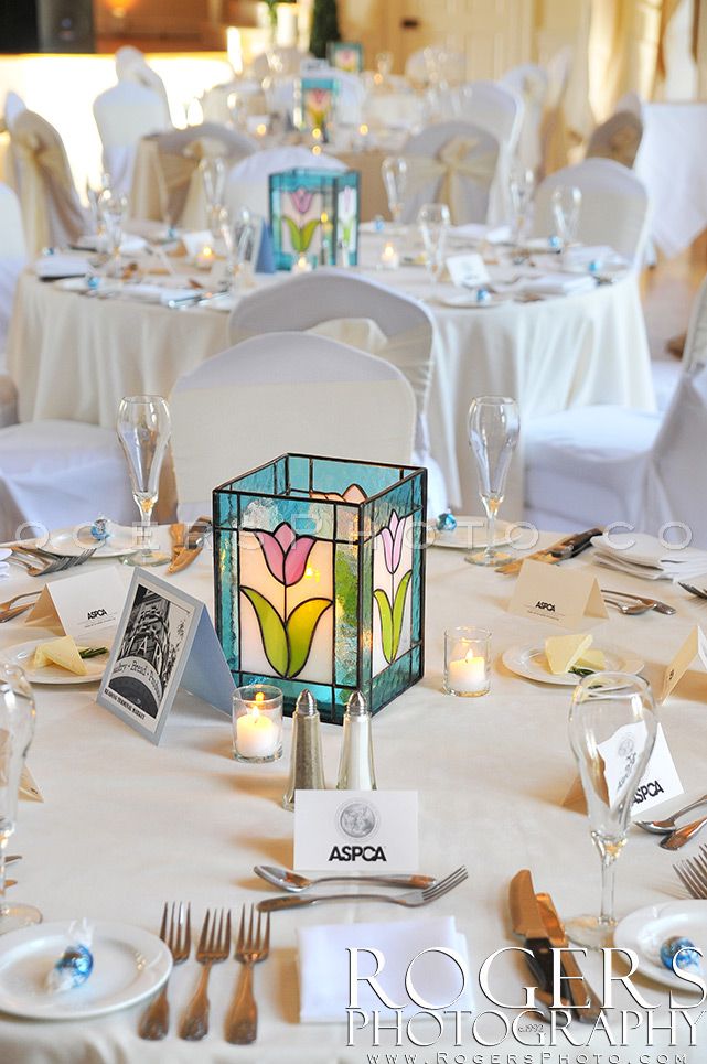 the table is set with white linens, silverware and colorful glass vases