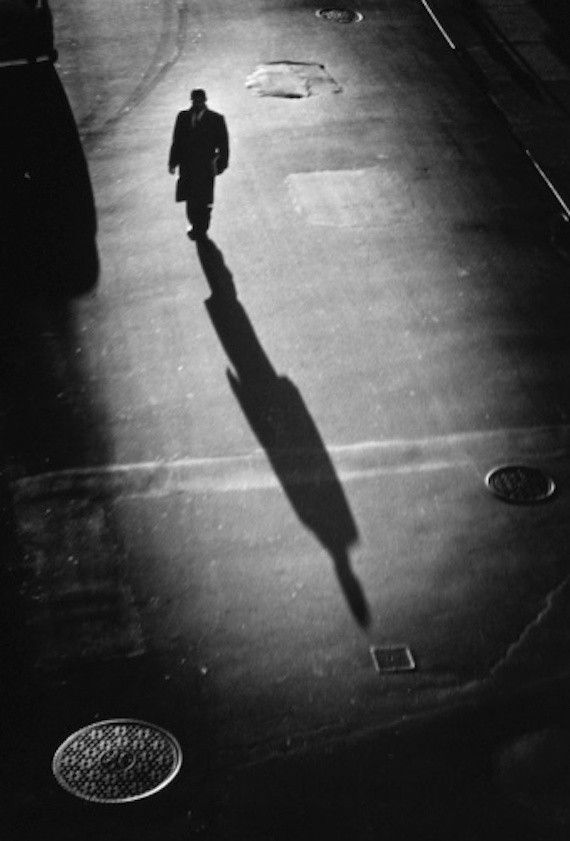 a man is walking down the street with his shadow on the ground in front of him