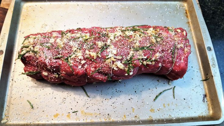 a piece of raw meat on a baking sheet with herbs and seasoning sprinkles