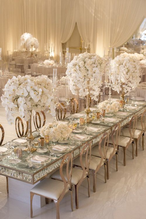 the tables are set up with white flowers and gold vases for centerpieces