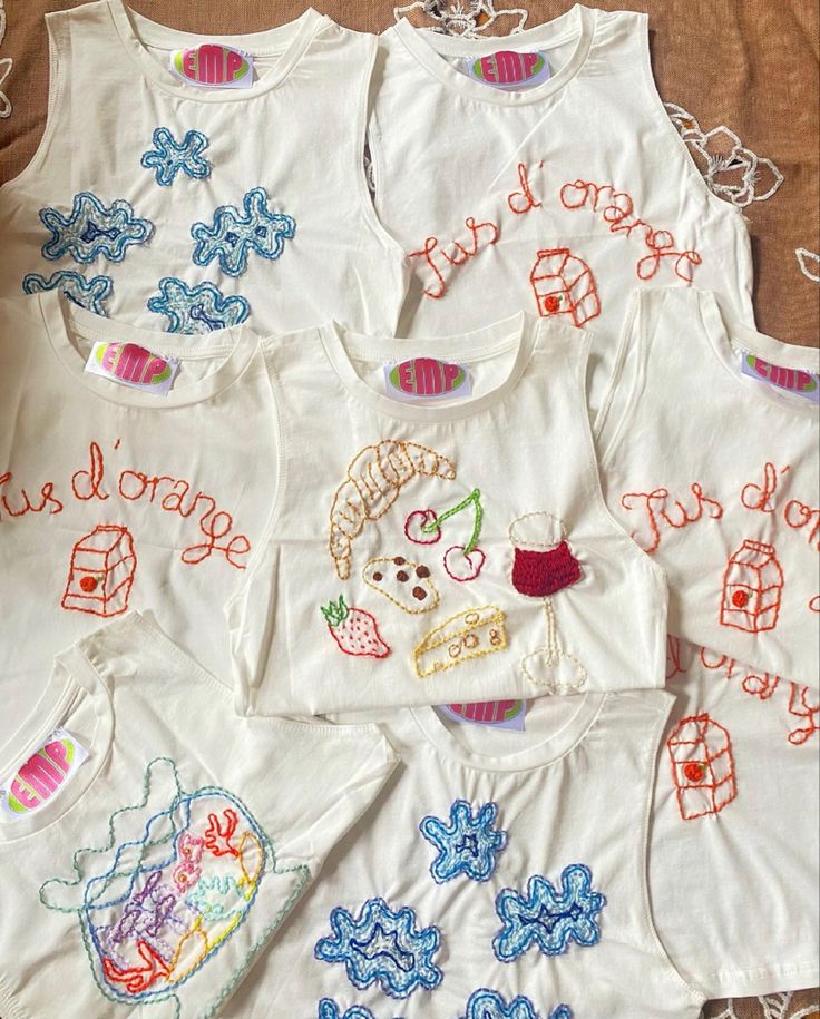 several white shirts with embroidered designs on them