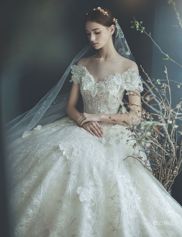 a woman in a white wedding dress sitting on a chair wearing a veil and flowers