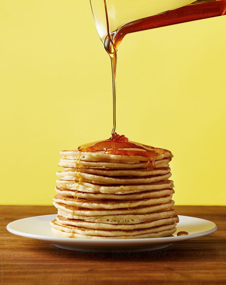 a stack of pancakes with syrup being poured onto them on a white plate against a yellow background