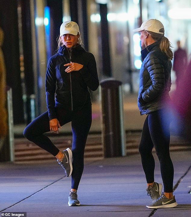 two women are standing on the sidewalk talking to each other while one is looking at her phone