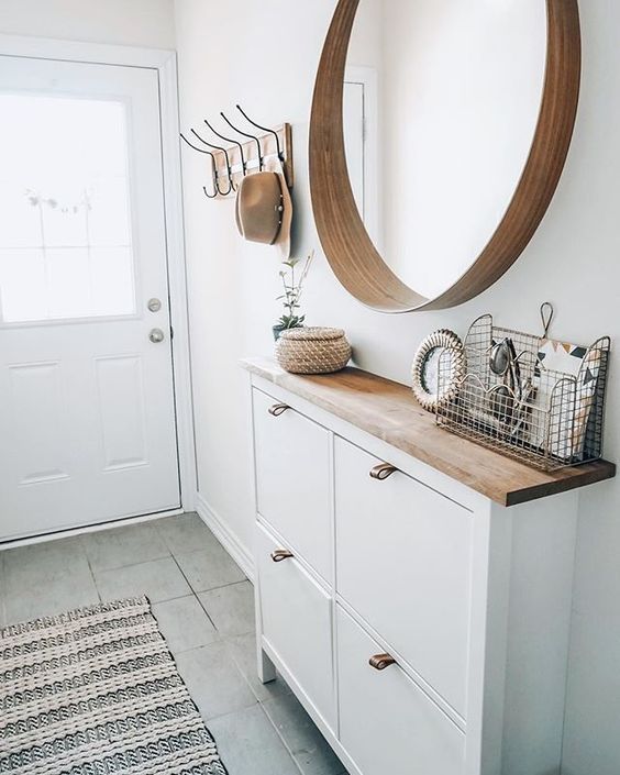 a white hallway with a wooden mirror and some hooks on the wall next to it