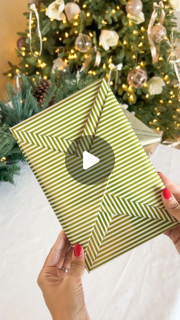 a woman holding up a christmas present in front of a tree