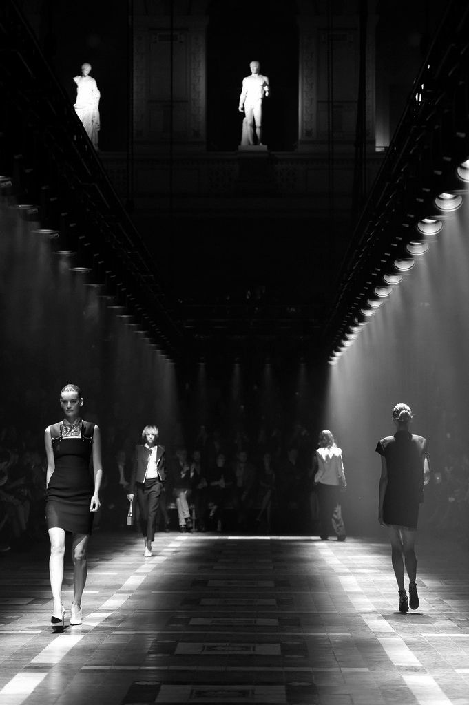 models walk down the runway in black and white outfits with spotlights on their faces