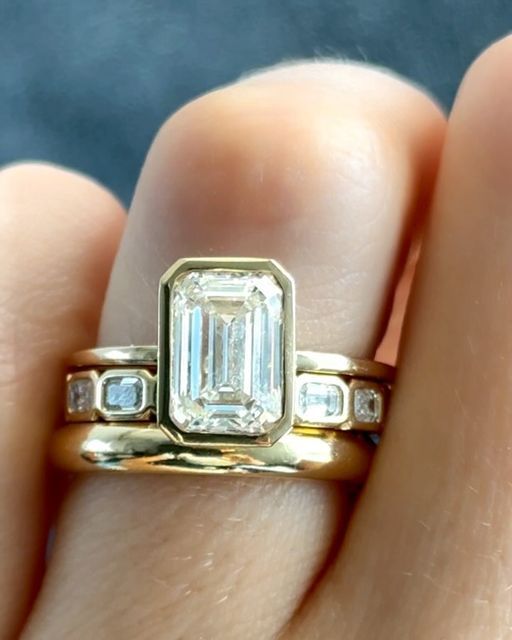 a close up of a person's hand holding a ring with an emerald and diamond