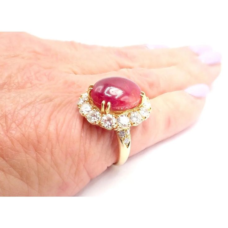 a woman's hand wearing a ring with a red stone and diamonds on it