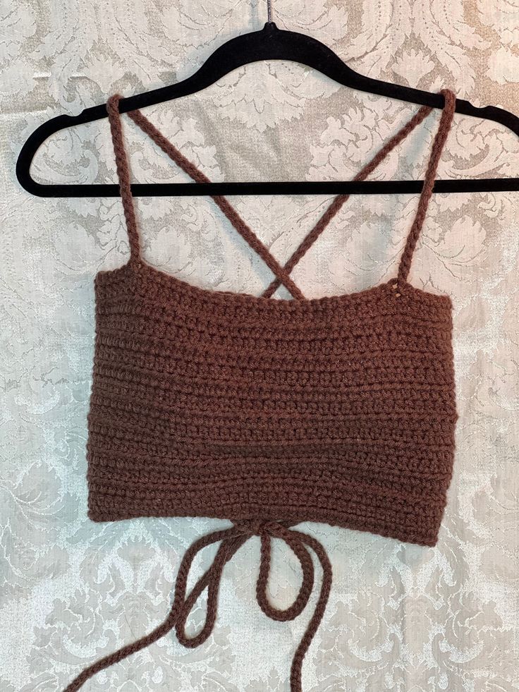 a brown crocheted top hanging on a hanger with white wallpaper in the background