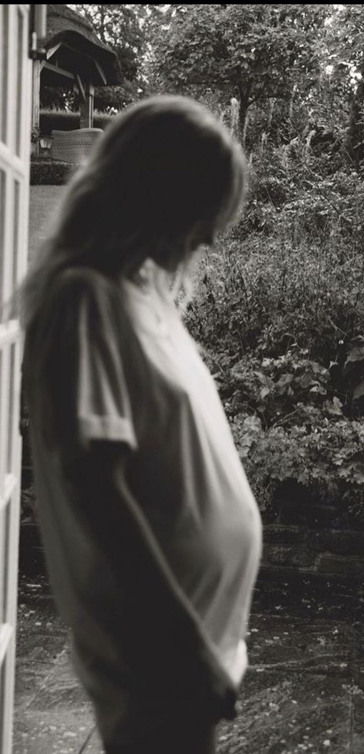 a pregnant woman standing in front of a window looking out at the yard and trees