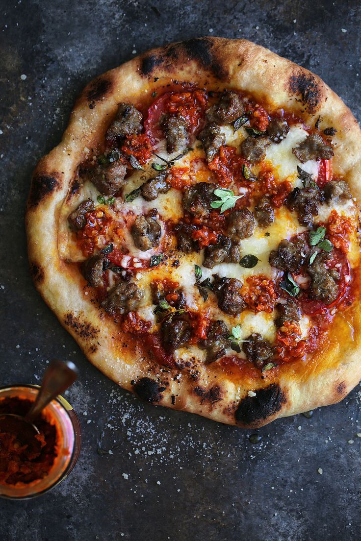 a pizza sitting on top of a pan covered in cheese and toppings next to a small bowl of sauce