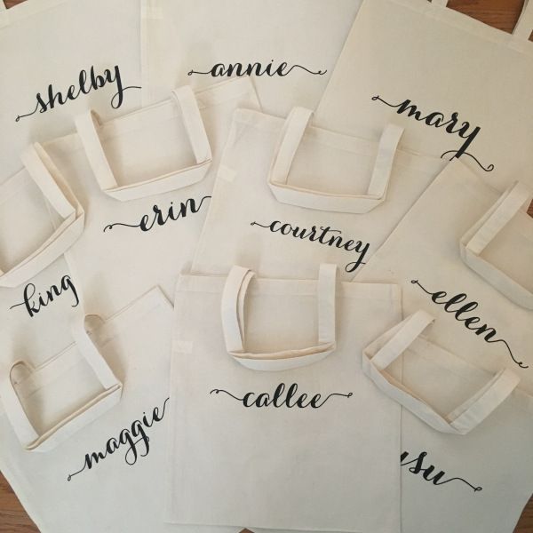 six tote bags with names on them sitting on a wooden table next to each other