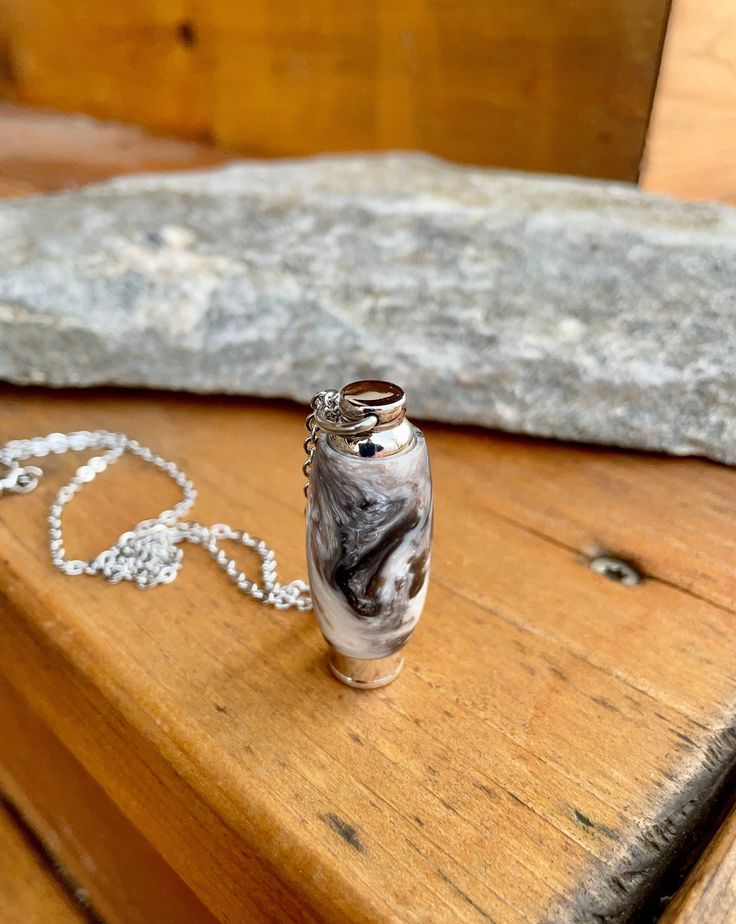 a small glass bottle sitting on top of a wooden table next to a silver chain