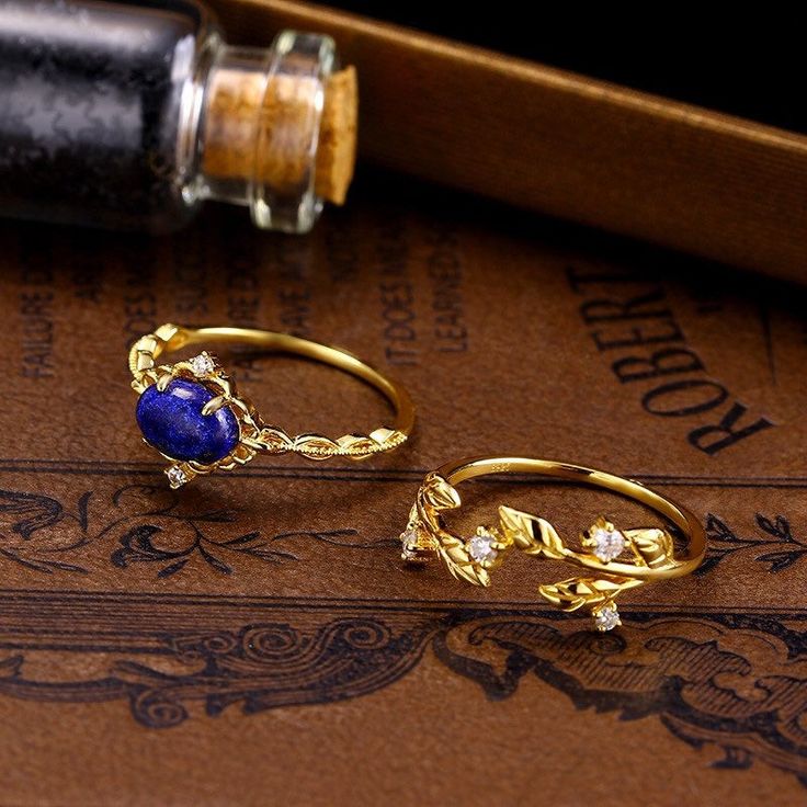 Bellucci Lazurite Blue Stone Ornate Laurel Leaves Gold Vermeil Stacking Ring Set features a simple east-to-west blue lazurite solitaire ring, paired together with an opulent golden laurel leaf ring. Make a statement with this striking combination. ◊ Available in US Ring Size 5 to 8 ◊ This is a made to order ring which will take 2-3 weeks to make, don't worry, we will will keep you in the loop and message you before we ship out! ◊ 18k Gold Vermeil ◊ Genuine lazurite ◊ All of our jewelry is nickel Elegant Gold Rings With Tanzanite, Elegant Gold Tanzanite Rings, Elegant Royal Blue Gemstone Rings, Gold Tanzanite Gemstone Rings, Gold-plated Sapphire Jewelry For Anniversary, Gold Tanzanite Round Rings, Gold Sapphire Ring With Gemstone Accents, Exquisite Tanzanite Jewelry Ring, Gold Plated Sapphire Jewelry For Anniversary