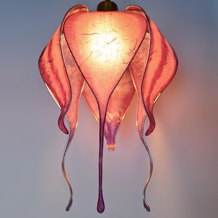 a pink lamp hanging from the side of a wall with an artistic design on it