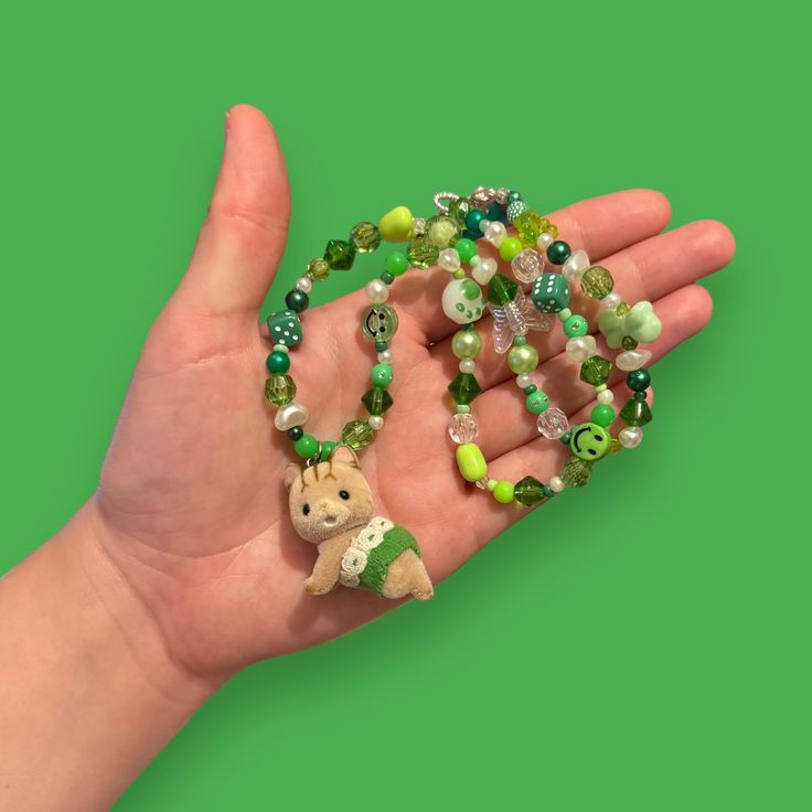 Bring some whimsy to your outfit with our Critter Bead Necklace, adorned with a charming Calico Critter. Each necklace is one-of-a-kind, handmade in Manchester, UK with varying colors and beads for a unique touch. Elastic thread and a clasp closure make it easy to wear. Cute Green Round Bead Jewelry, Green Beaded Necklace With Lobster Clasp As Gift, Playful Handmade Adjustable Charm Necklaces, Cute Handmade Green Beaded Necklaces, Cute Handmade Green Jewelry, Handmade Adjustable Whimsical Charm Necklace, Playful Beaded Necklace For Gift, Adjustable Whimsical Green Necklace, Whimsical Adjustable Beaded Chain Necklaces