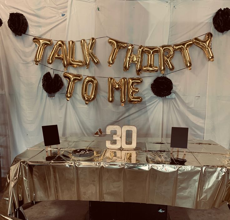 a table that has some balloons on it and the words talk about to me spelled in gold