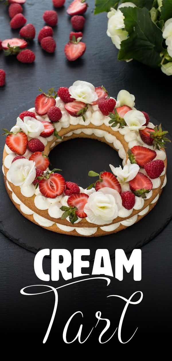 a cake decorated with strawberries and flowers on top of a black table next to white roses