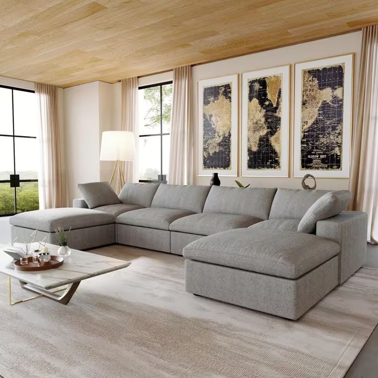 a living room with a sectional couch and coffee table in front of two large windows