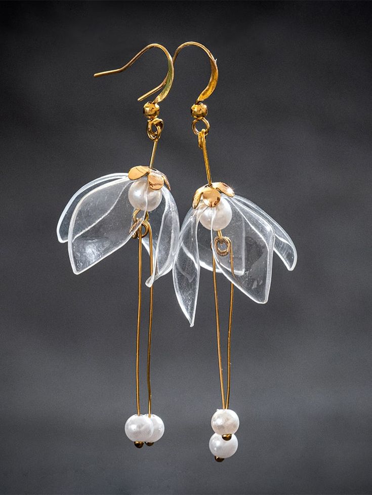 the earrings are made from clear plastic and gold - plated metal, with pearls hanging from them