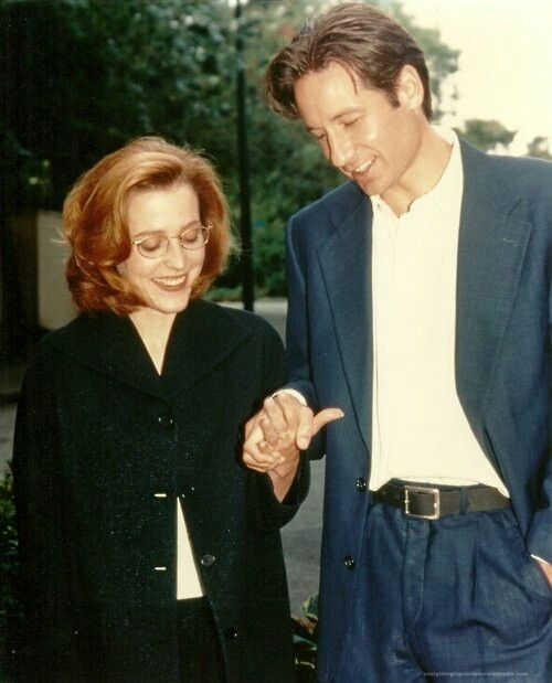 a man and woman standing next to each other on a sidewalk with trees in the background