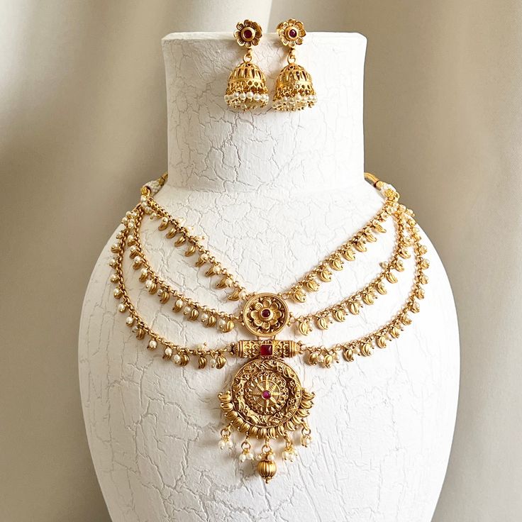 "Traditional antique gold ruby temple necklace set. Set includes: necklace and earrings. Earrings Length: 1.5\" | Width: 1\" Items are carefully packed and ready for gifting. All pictures are taken in natural light please allow for slight variations in color due to camera settings. Jewelry Care ✨Protect your jewelry in a closed box or pouch   ✨Wear jewelry after you have applied lotion or perfume ✨Gently buff with a soft cotton cloth  Visit our website: www.desimoon.etsy.com Thank you for visiti Gold Plated Round Temple Necklace, Antique Gold Temple Jewelry Bridal Necklace, Temple Jewelry Gold Jewelry Set For Puja, Gold Plated Temple Jewelry Sets, Gold Temple Jewelry Set For Puja, Temple Jewelry Sets With Latkans And Round Shape, Gold Ruby Temple Jewelry Bridal Necklace, Antique Gold Temple Necklace For Wedding, Antique Gold Temple Necklace For Celebration