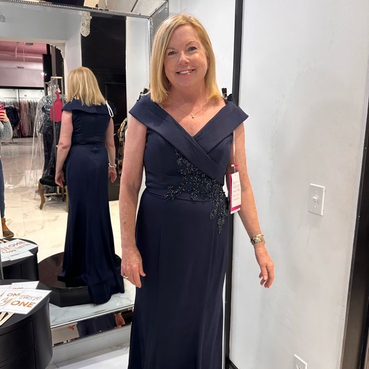 a woman standing in front of a mirror wearing a blue dress with an asymmetrical neckline