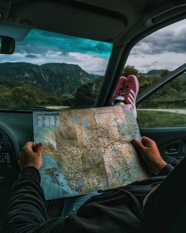 a person sitting in the passenger seat of a car looking at a map with mountains in the background