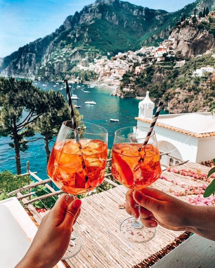 two people holding up wine glasses with water in the background