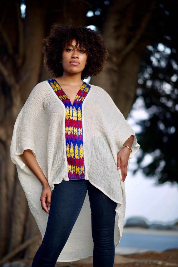 Boldly Cozy With A Boho Twist. Simply-Chic Layering piece, that dresses up or down for any occasion.• V-Neck and flattering drape• 100% Cotton • V-neck • Embroidery By Hand In Ethiopia. • Made in California.• size one size fits most { the size is loose fit it well fit from size 2 to size 12 } • front length 23” from the shoulder. • Machine wash In Delicate cycle or hand was in cold water. Tumble dry low heat for crinkle look. • Color off white / beige/ the embroidery is multi color. Casual White Cotton Poncho, Free Size Short Sleeve Blouse, Casual White Poncho With Batwing Sleeves, Short Sleeve Poncho For Vacation, Casual White Short Sleeve Kaftan, Casual Free Size Top With Batwing Sleeves, Oversized Tunic Top For Vacation, Casual Free Size Batwing Sleeve Tops, White Oversized Casual Poncho