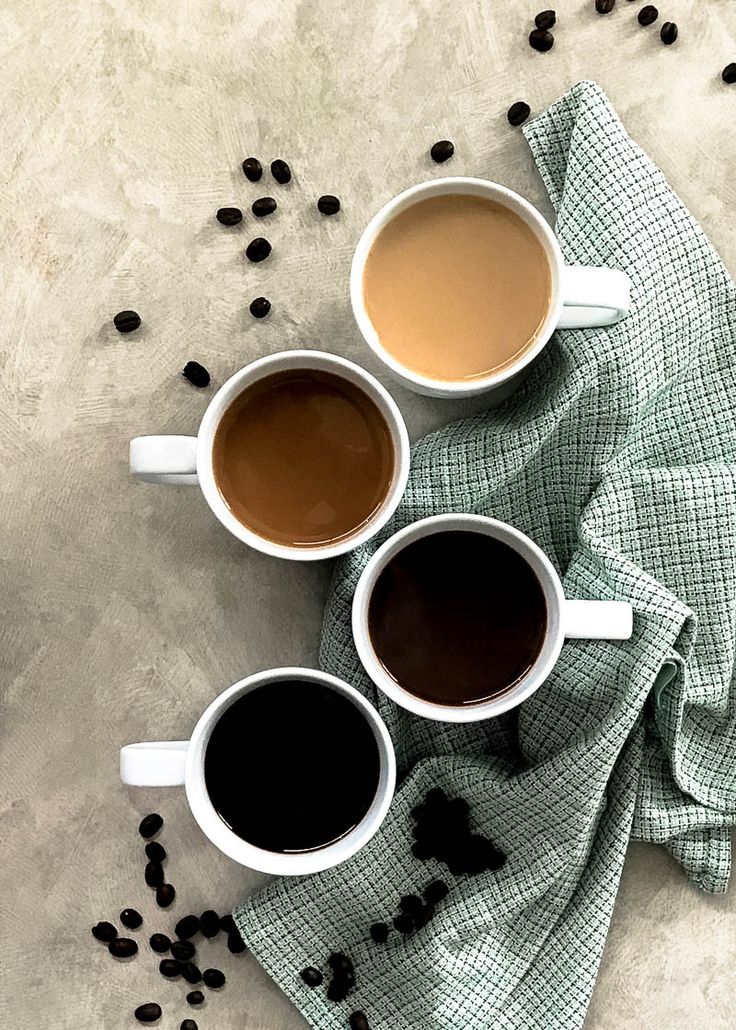 three cups of coffee sitting on top of a green towel next to some black beans