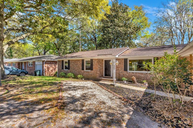 a brick house with trees in the front yard and two cars parked on the driveway