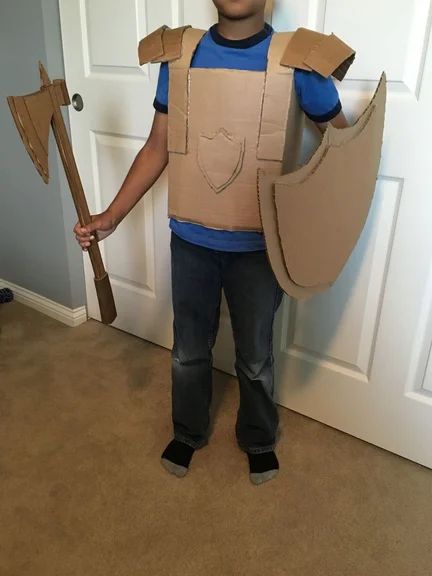 a young boy wearing a cardboard costume and holding a wooden stick