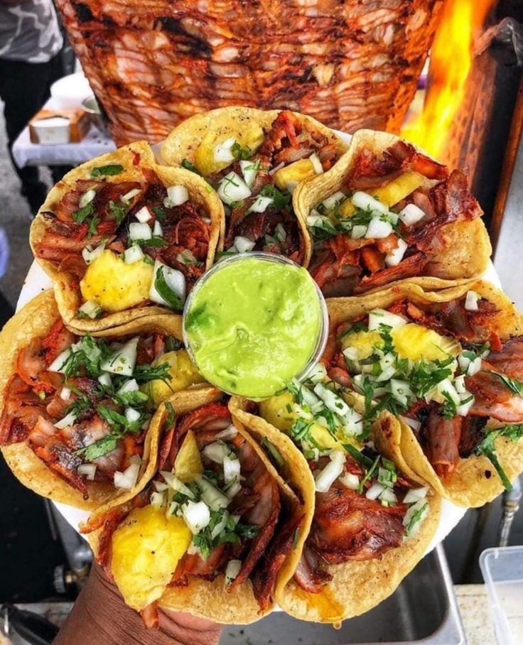 a person holding up a plate with tacos and guacamole