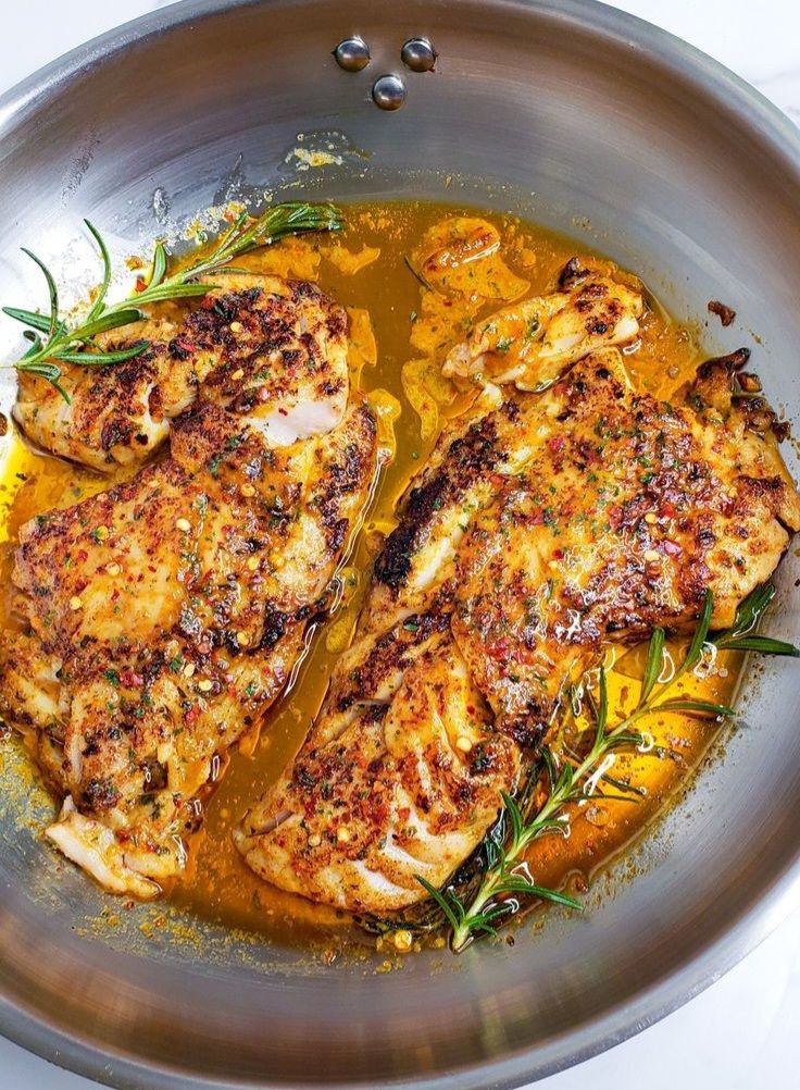 two pieces of chicken are in a pan with some herbs on the side and seasoning