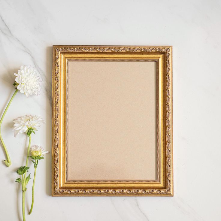 a gold frame sitting on top of a white counter next to flowers