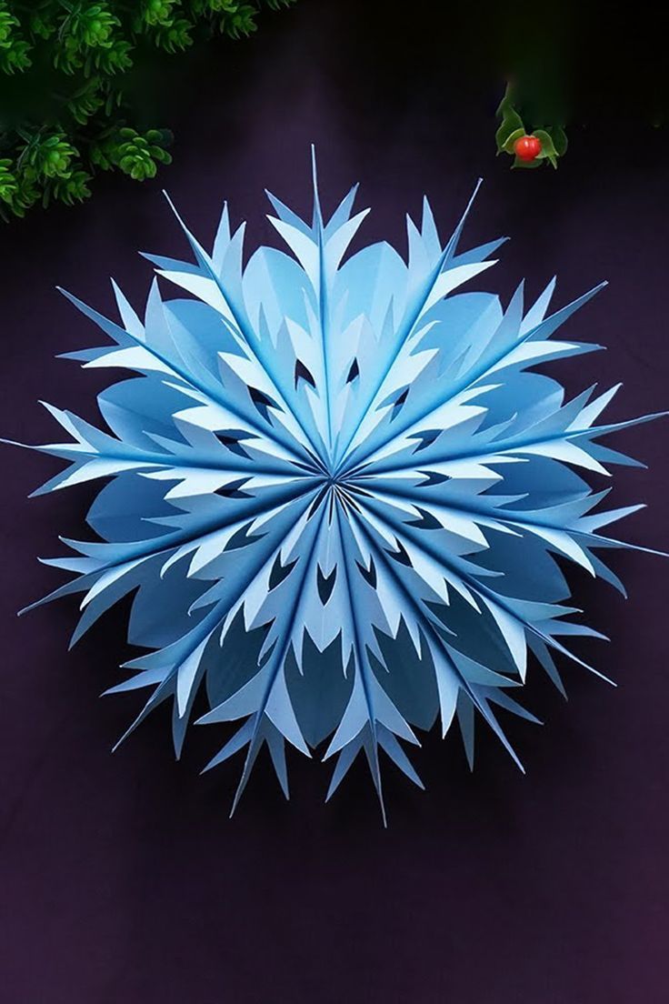 an overhead view of a paper snowflake on a purple surface with green plants in the background