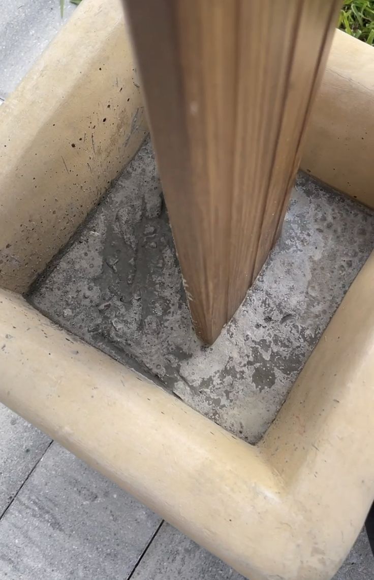 a wooden pole sticking out of the ground in front of a cement floor and grass area