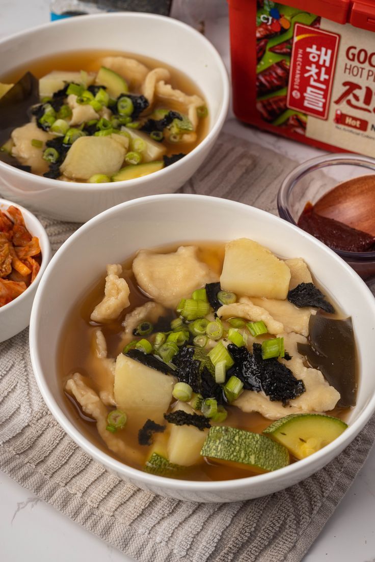 two white bowls filled with soup and vegetables on top of a table next to a box of food