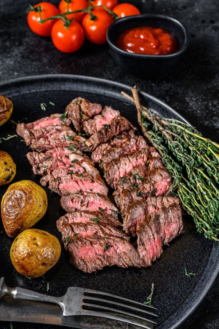 steak, potatoes and tomatoes on a black plate