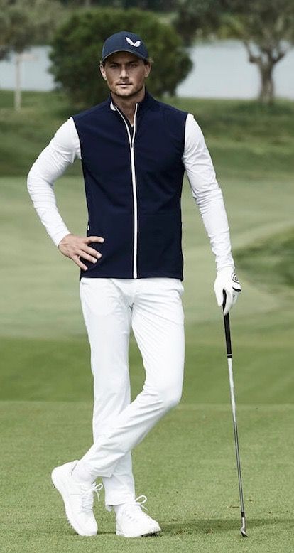 a man standing on top of a green golf course holding a golf club and wearing white pants