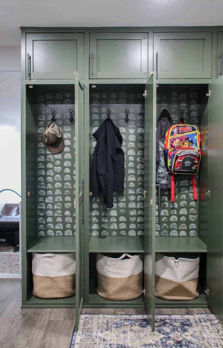 a green locker with two coats hanging on the wall and three bags in front of it