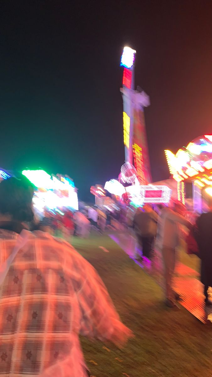 blurry photograph of people walking around an amusement park at night with rides and carnival booths in the background