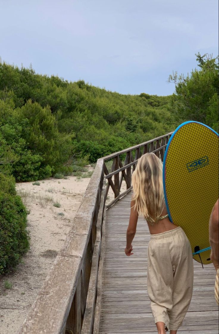 a woman walking across a bridge carrying a surfboard