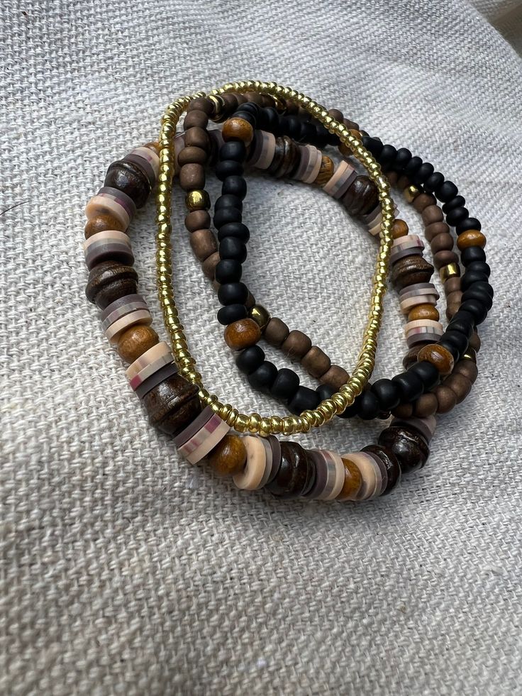 Mixed wood, glass, and clay beads. Brown, black, and gold tones. Stretch bracelet set of 4. Set includes all 4 bracelets shown. Brown Heishi Beads Bracelet, Brown Heishi Beads Bracelet With Colorful Beads, Brown Heishi Beads Bracelets With Colorful Beads, Brown Beaded Heishi Bracelets, Adjustable Brown Beaded Bracelets With Black Beads, Adjustable Brown Heishi Beads, Casual Brown Bracelet With Black Beads, Casual Brown Bracelets With Black Beads, Bohemian Brown Beaded Bracelets With Gold Beads