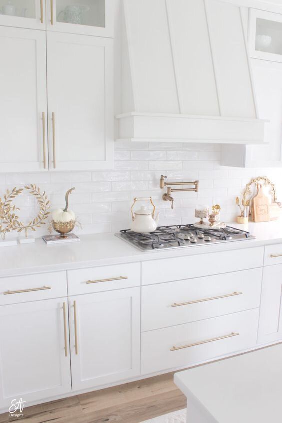 a kitchen with white cabinets and gold trim on the hood, stove top and oven