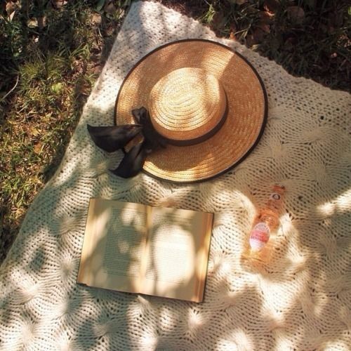 a hat, book and other items on a blanket in the shade outside by some trees