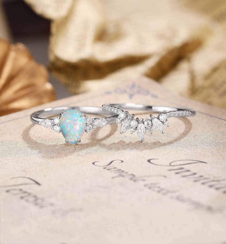 an opal and diamond ring sitting on top of a table next to a book