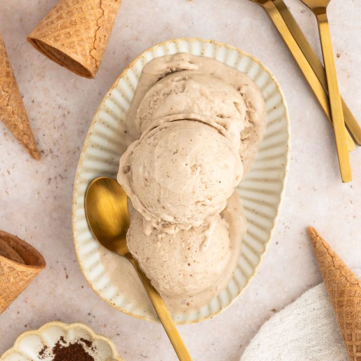 two scoops of ice cream sit on a plate with spoons next to it